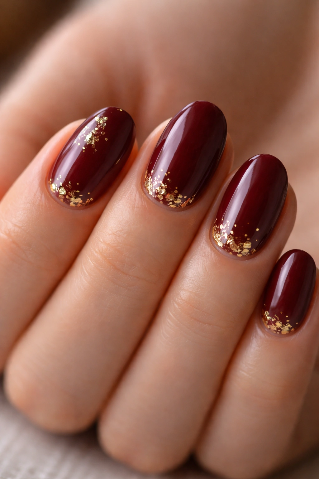 Short oval maroon nails with tiny gold foil accents