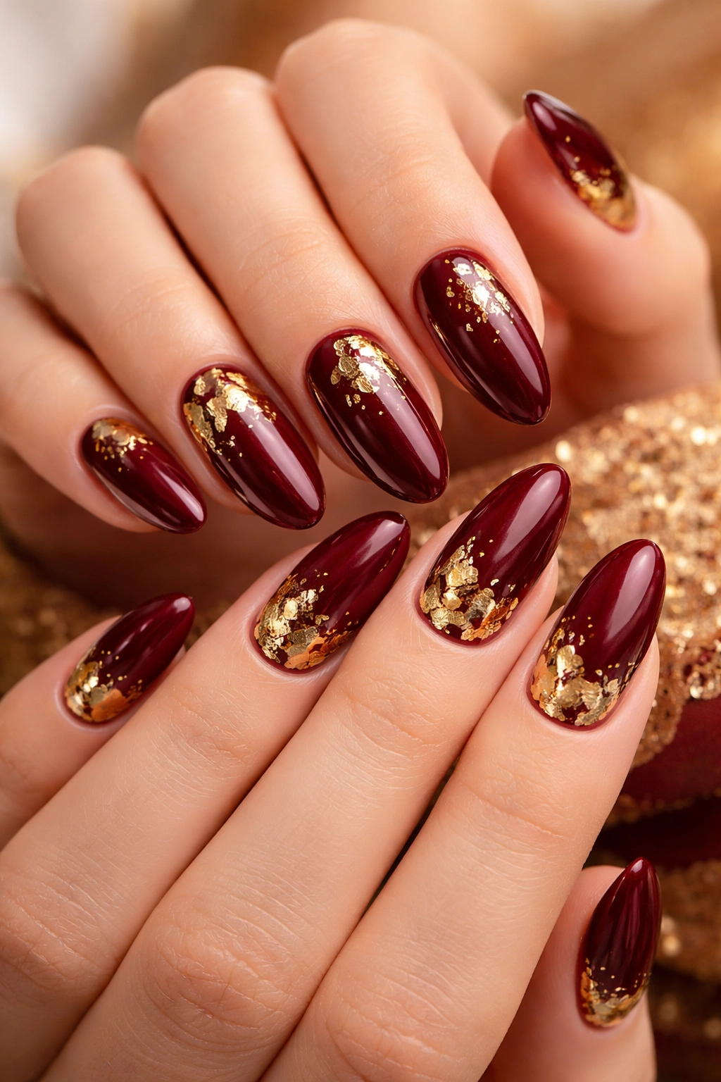 Close-up of maroon nails with gold foil accents on a neutral background