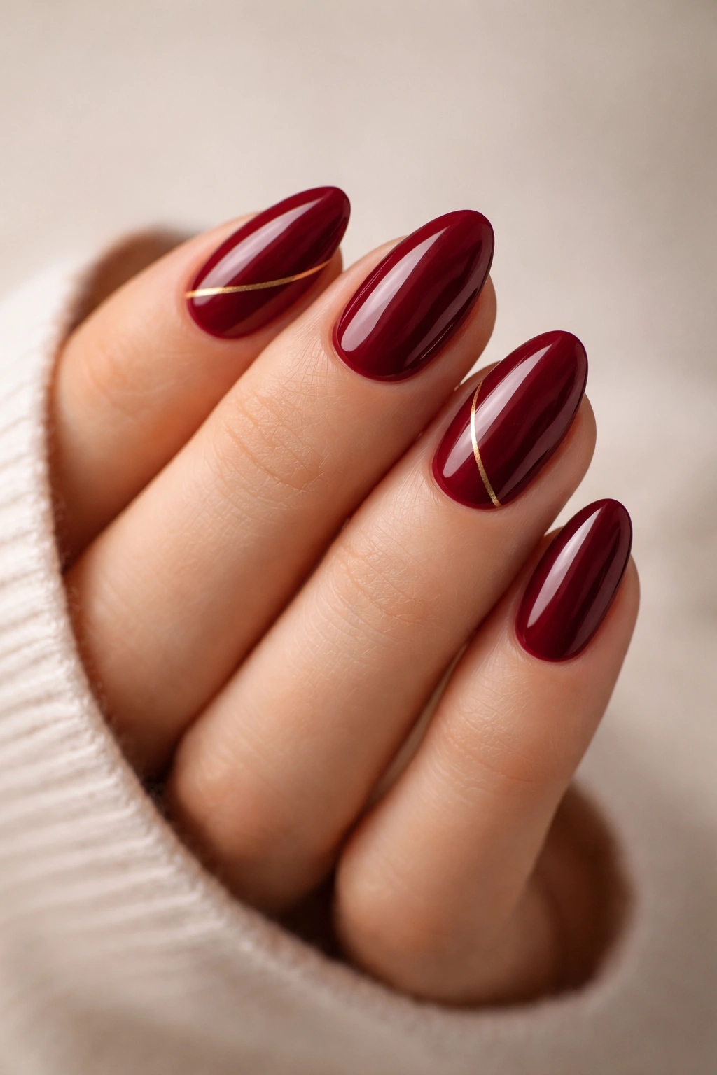 Close-up of short almond nails maroon with thin gold line accents