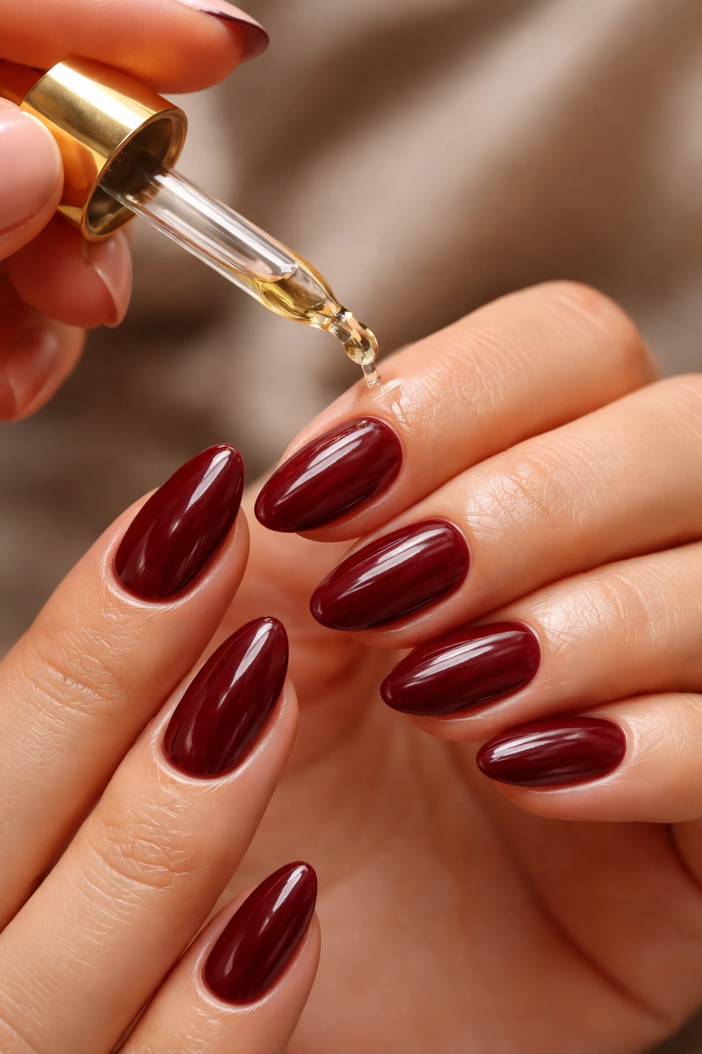 Hands applying cuticle oil to short almond maroon nails