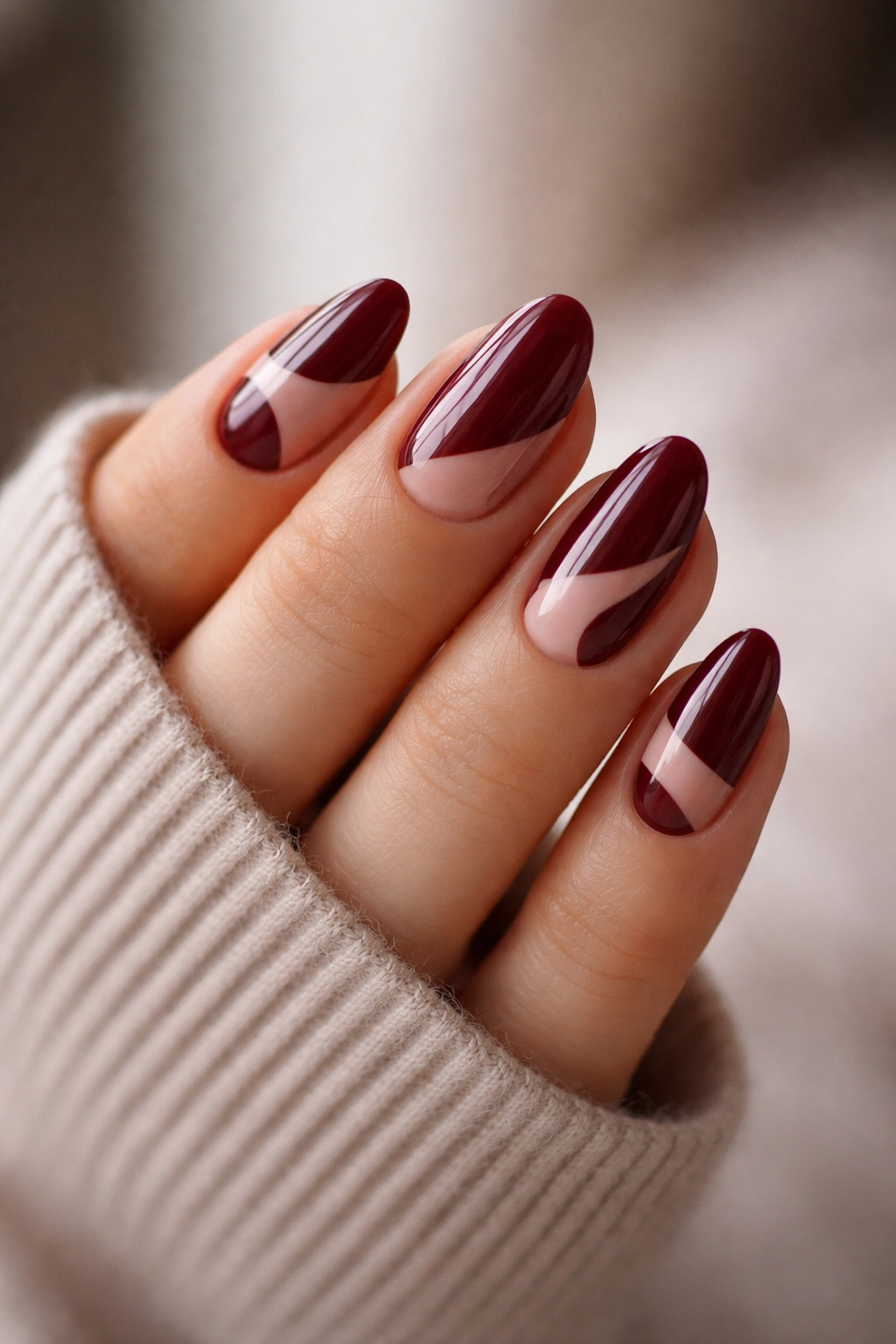 Close-up of short almond nails in maroon polish with negative-space cutouts on a clean background
