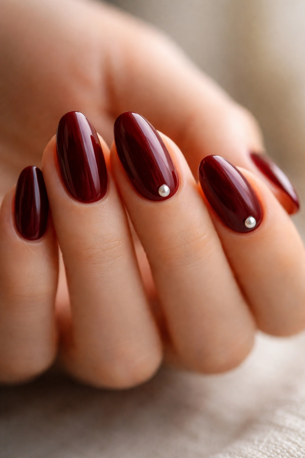 Short almond nails with maroon base and tiny pearl accents