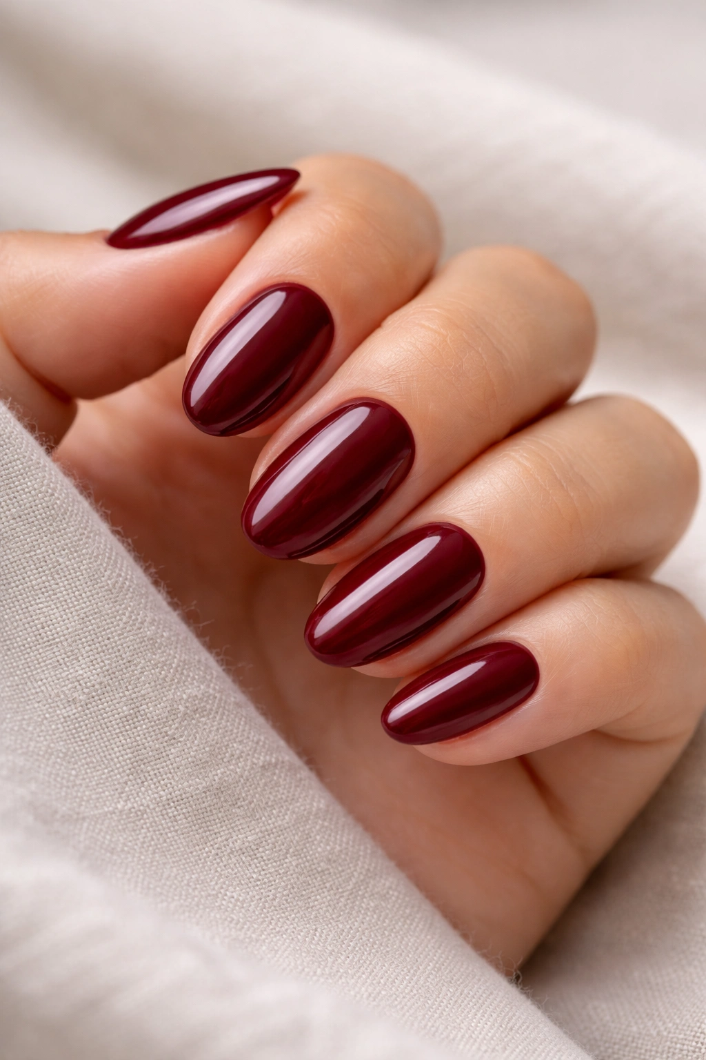 Close-up of short almond nails in deep maroon with a high-gloss finish