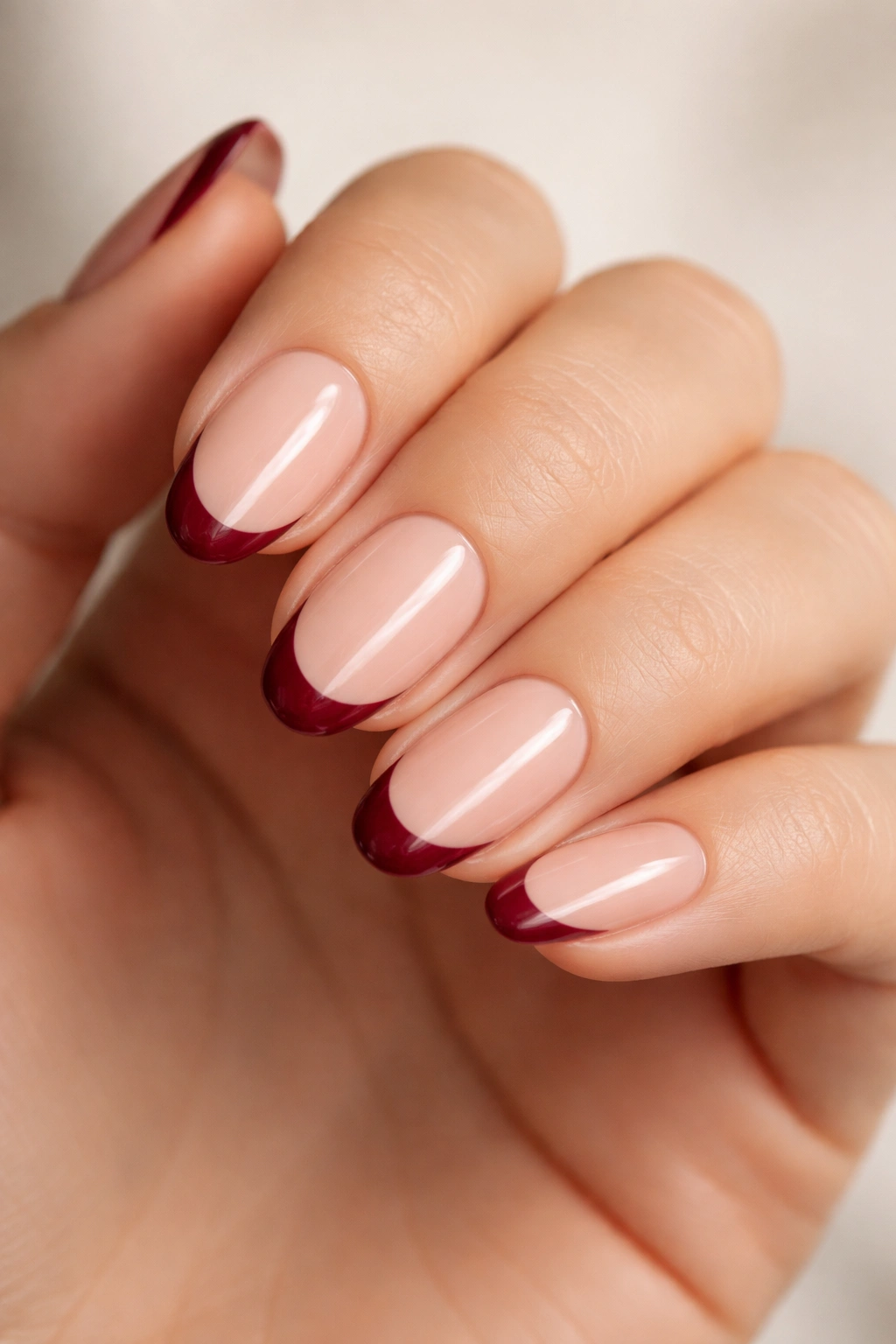 Close-up of maroon French tips on nude base on short almond nails