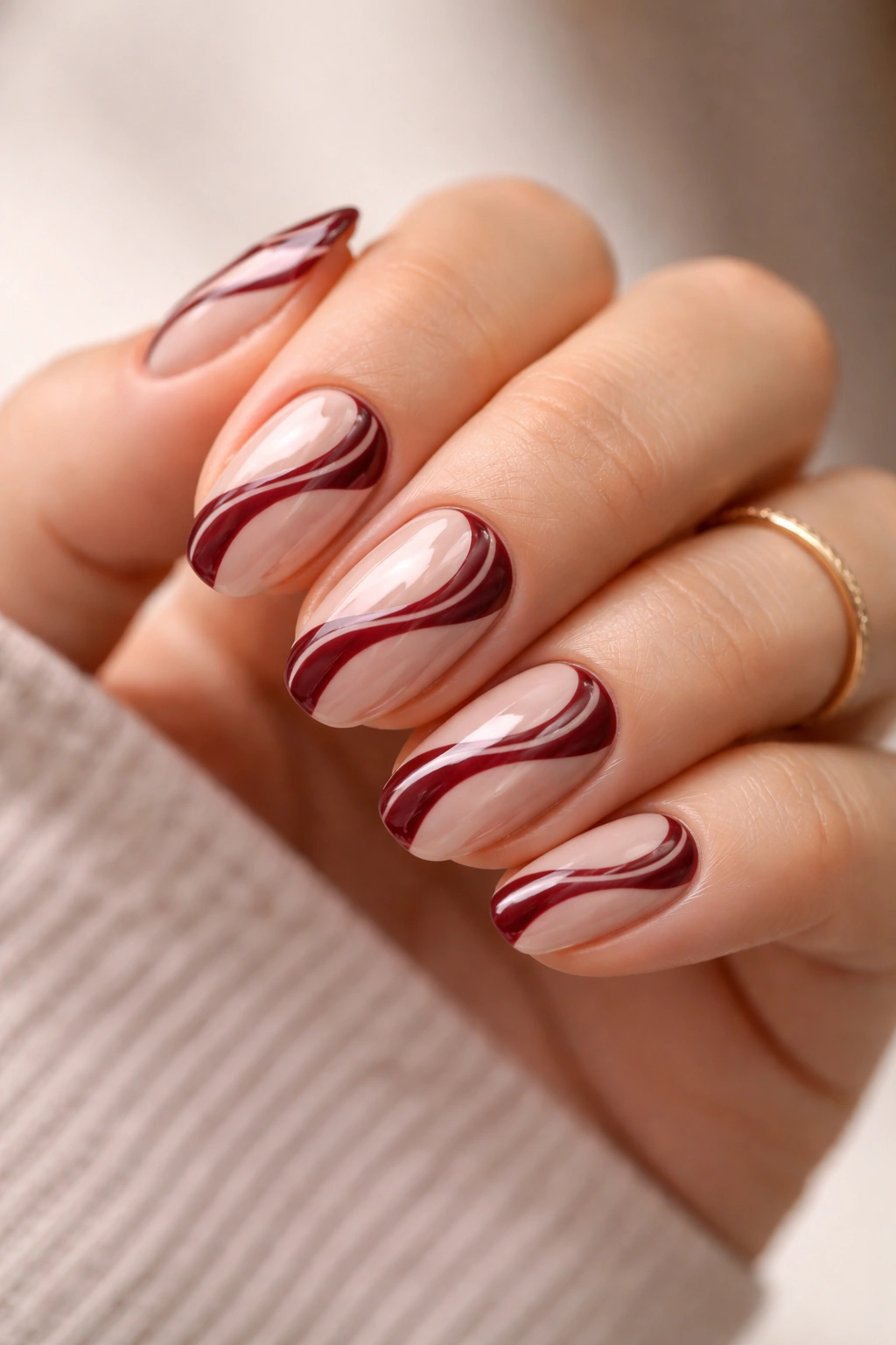 Close-up of maroon and nude swirl nails on short ovals with flowing curves