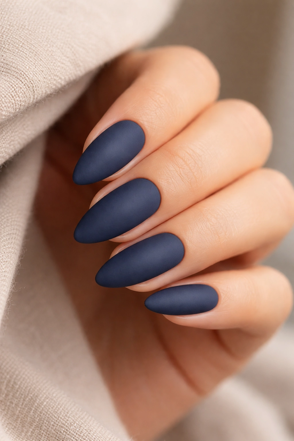 Close-up of matte almond nails in deep navy on neutral background