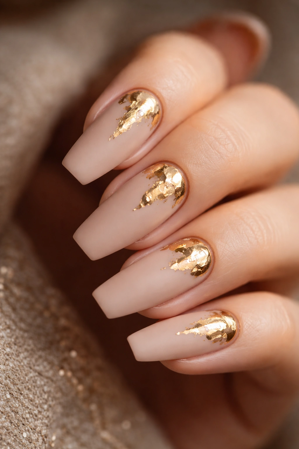 Close-up of matte beige ballerina nails with irregular glossy gold foil fragments