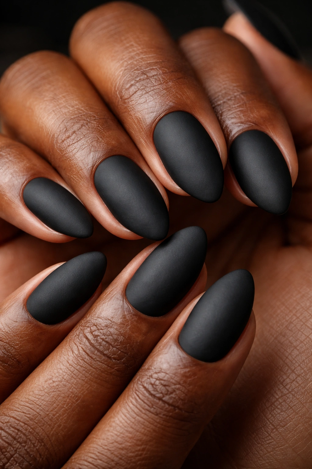 Close-up of matte black almond nails with velvety finish on dark skin