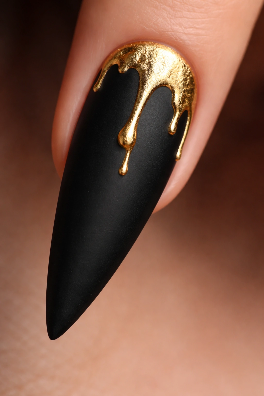 Close-up of a matte black stiletto nail with a gold drip