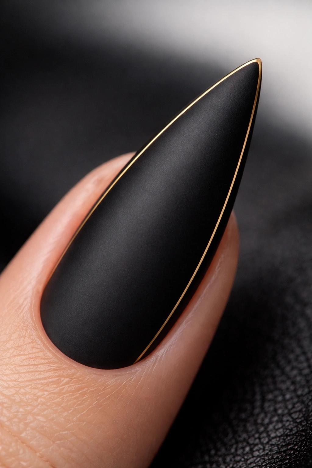 Matte black stiletto nail with a thin gold outline