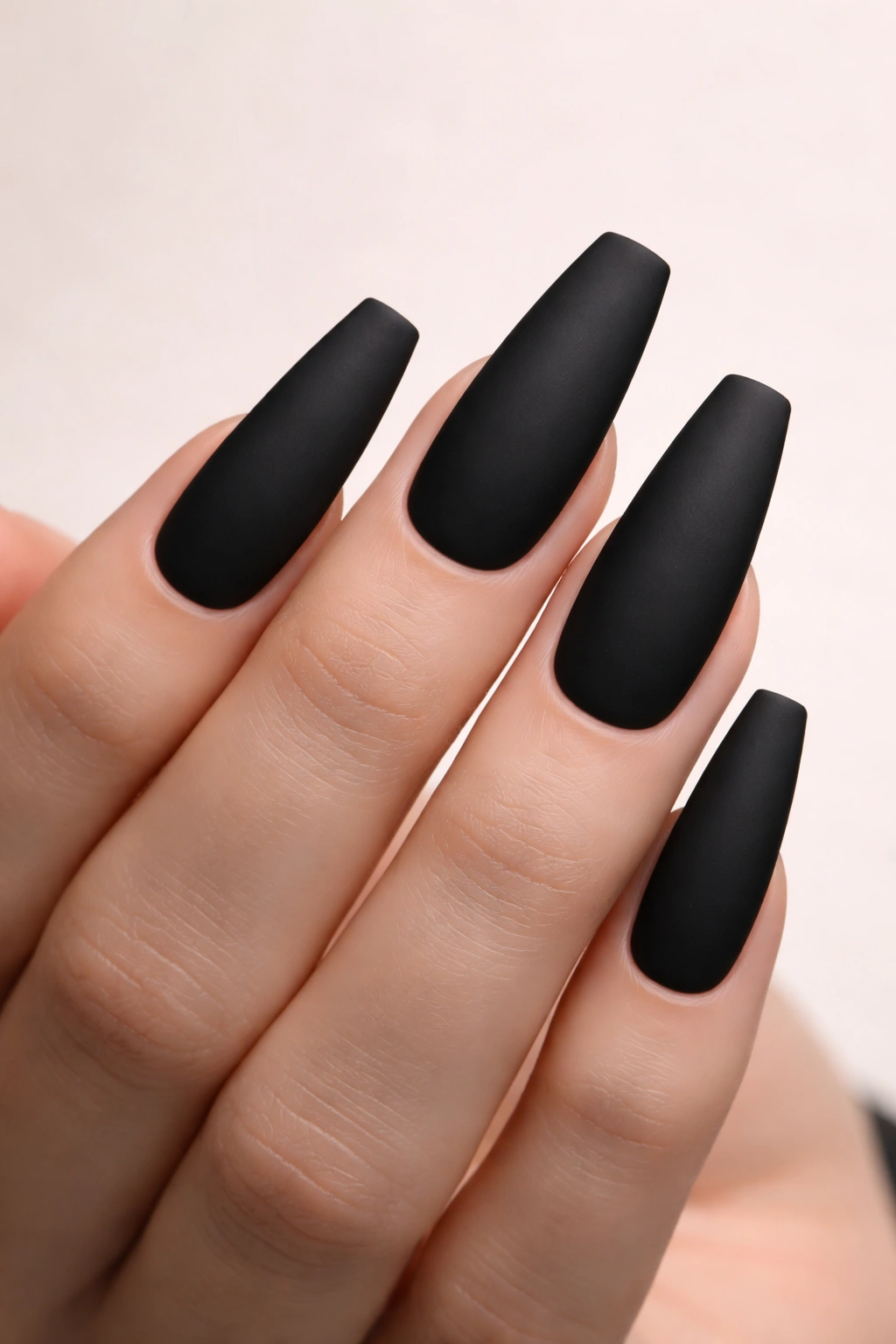 Close-up of coffin-shaped matte black acrylic nails on a neutral background.