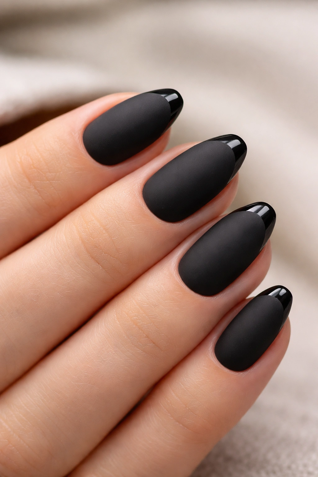 Close-up of short almond nails with matte base and thin glossy tips.