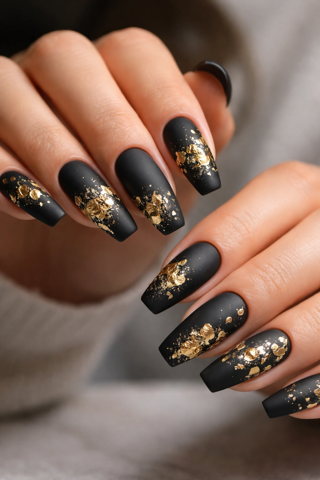 Close-up of coffin nails with matte black finish and irregular gold leaf accents