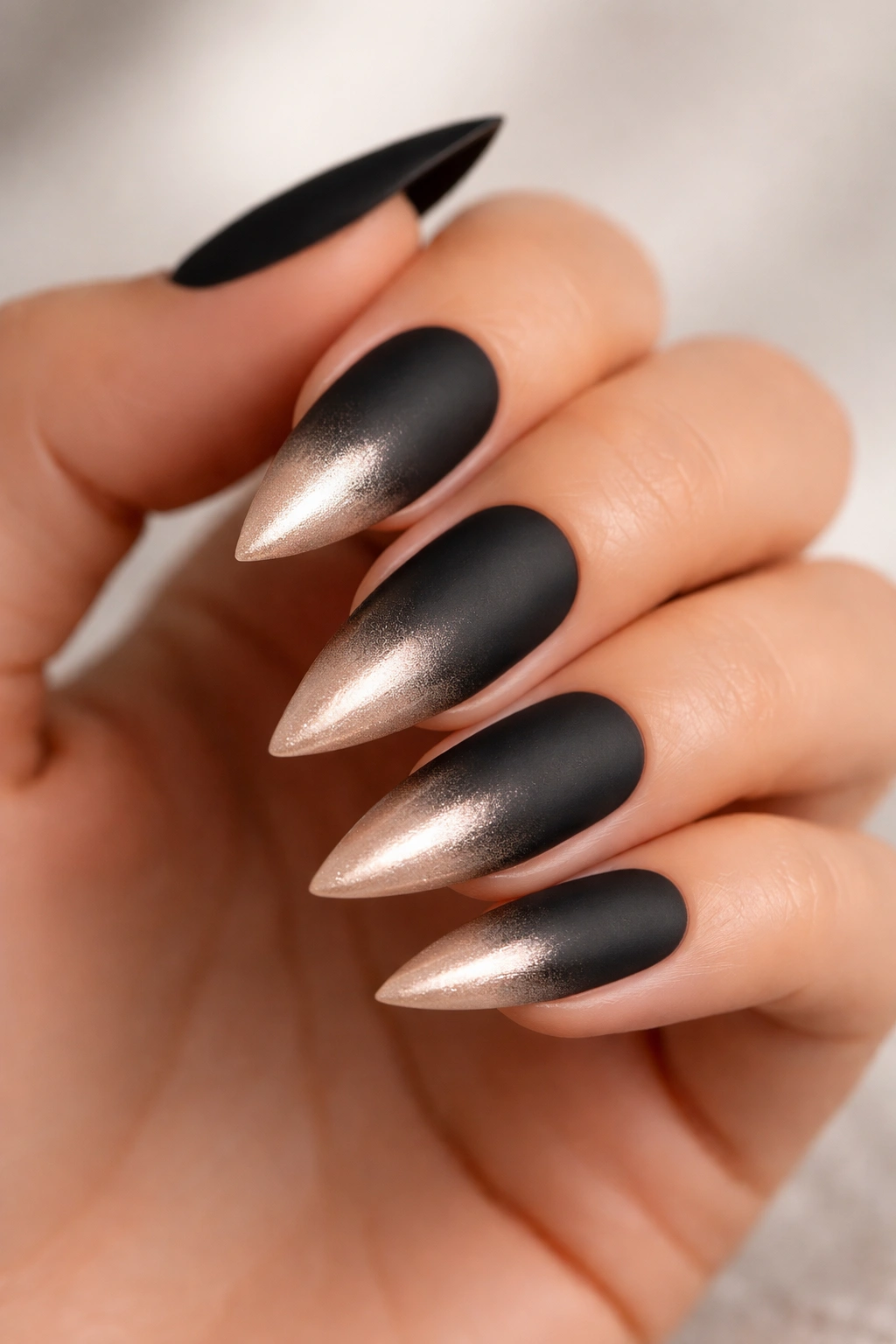 Close-up of matte black to metallic nude gradient on medium-length stiletto nails