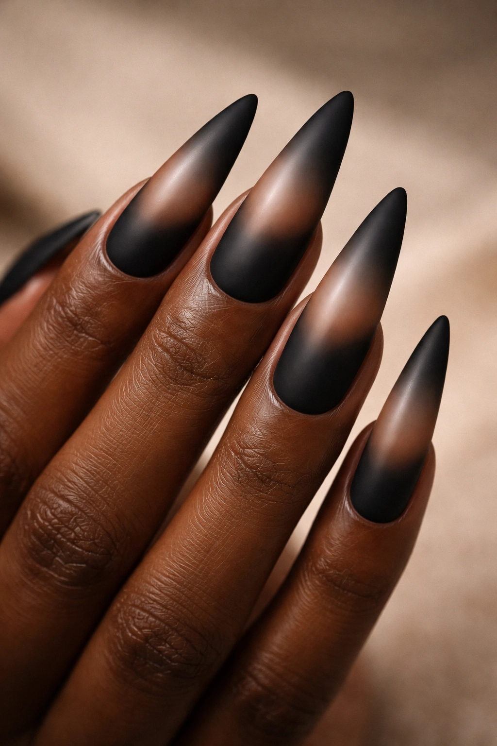 Close-up of matte black stiletto nails with nude gradient tips on a neutral background