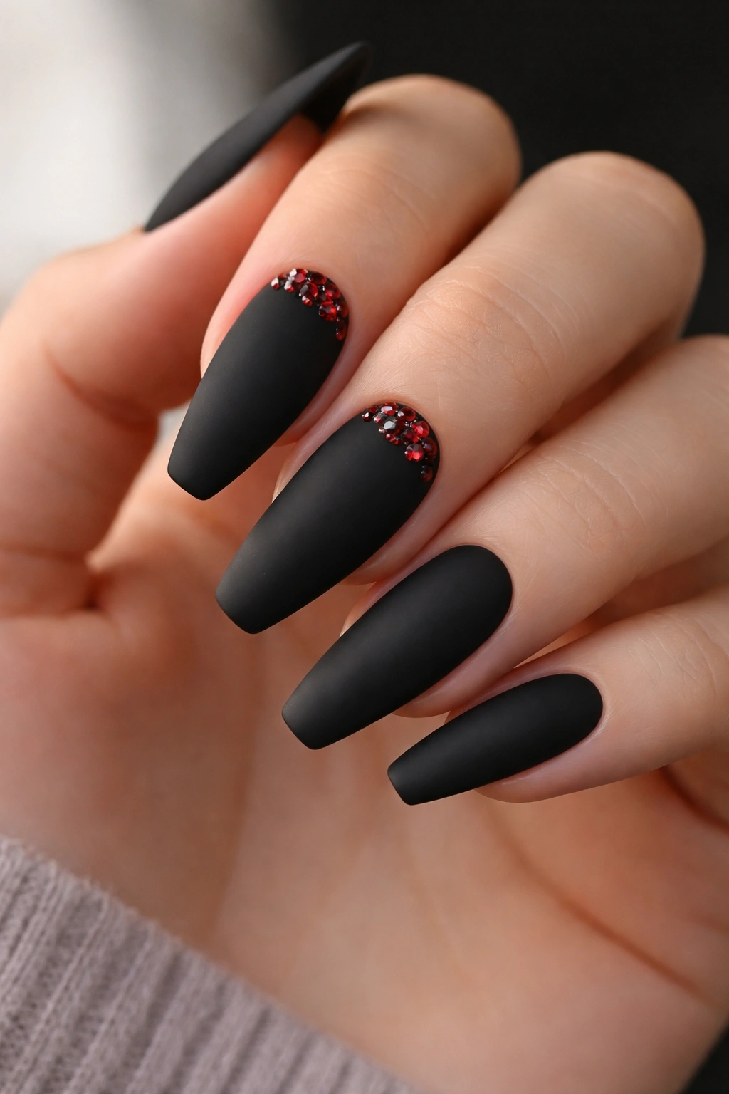 Matte black nails with tiny red gem clusters near the cuticle on two nails
