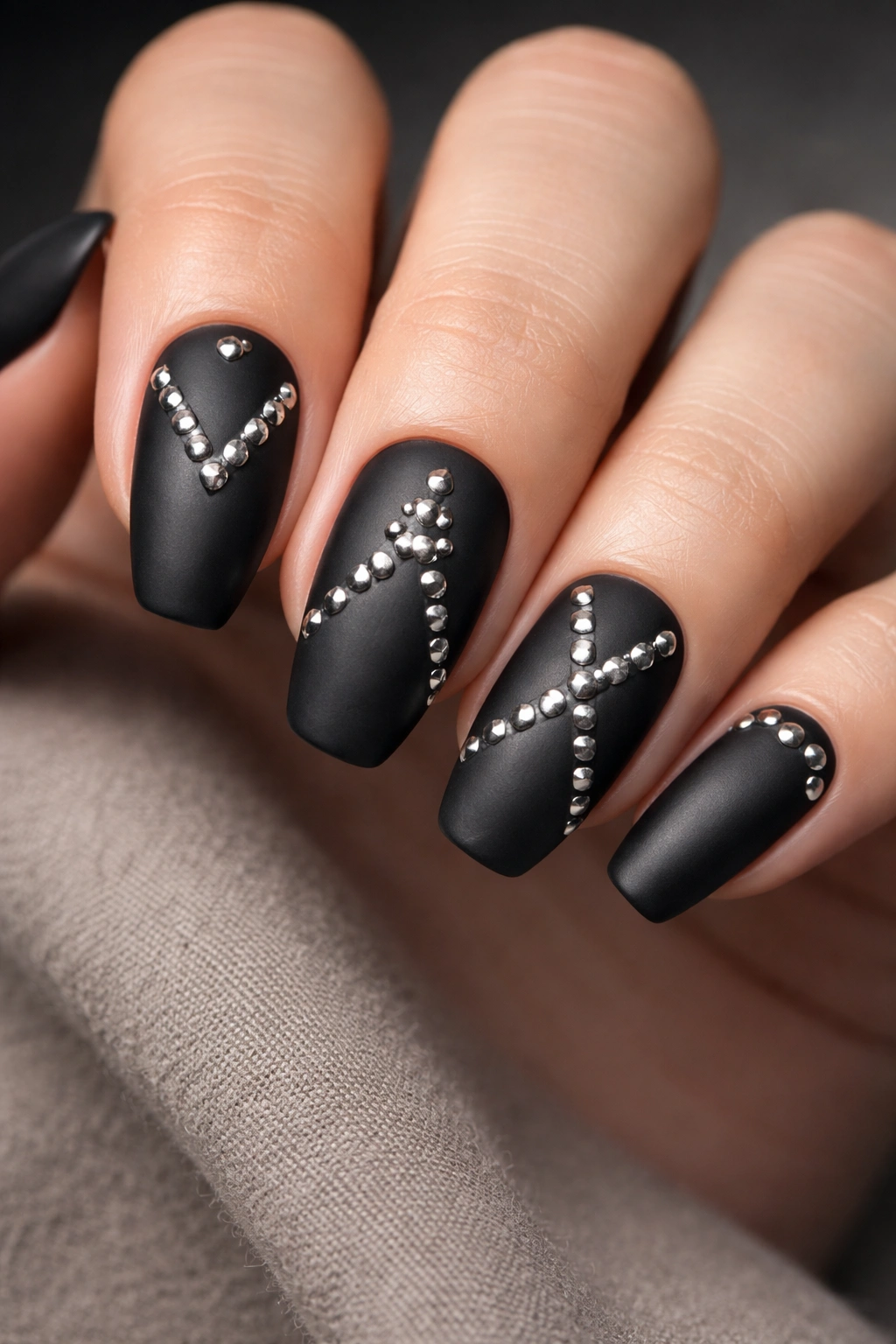 Close-up of matte black nails with silver studs in geometric pattern