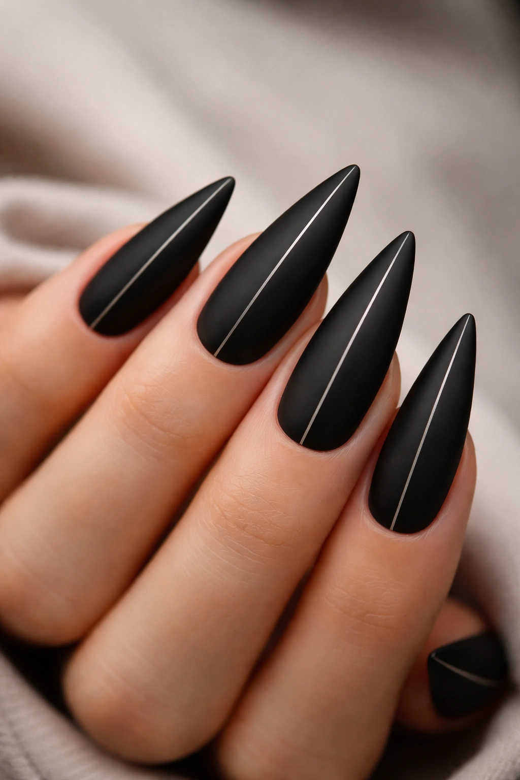 Close-up of matte black stiletto nails with a single center line.