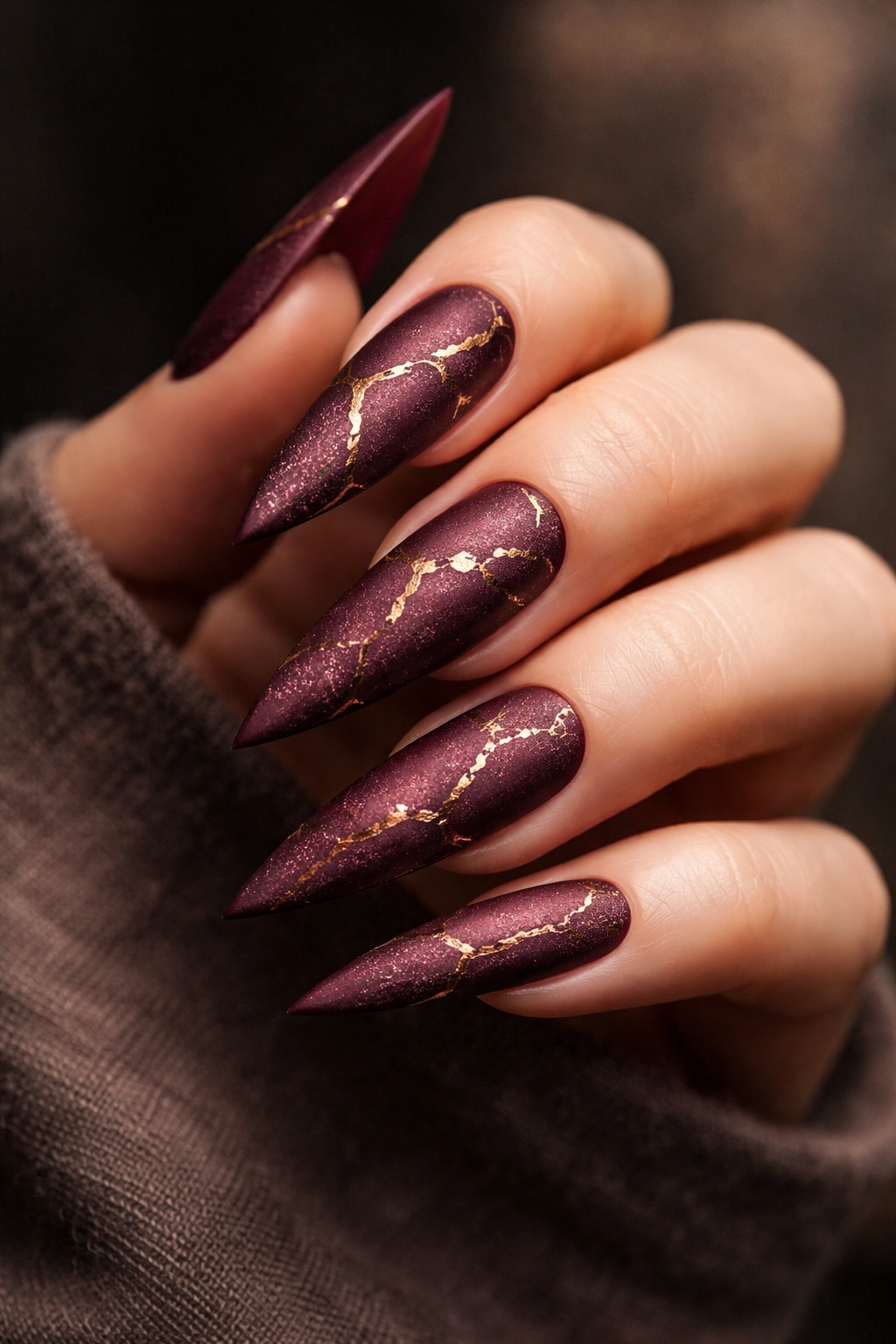 Close-up of matte burgundy stiletto nails with gold crack accents