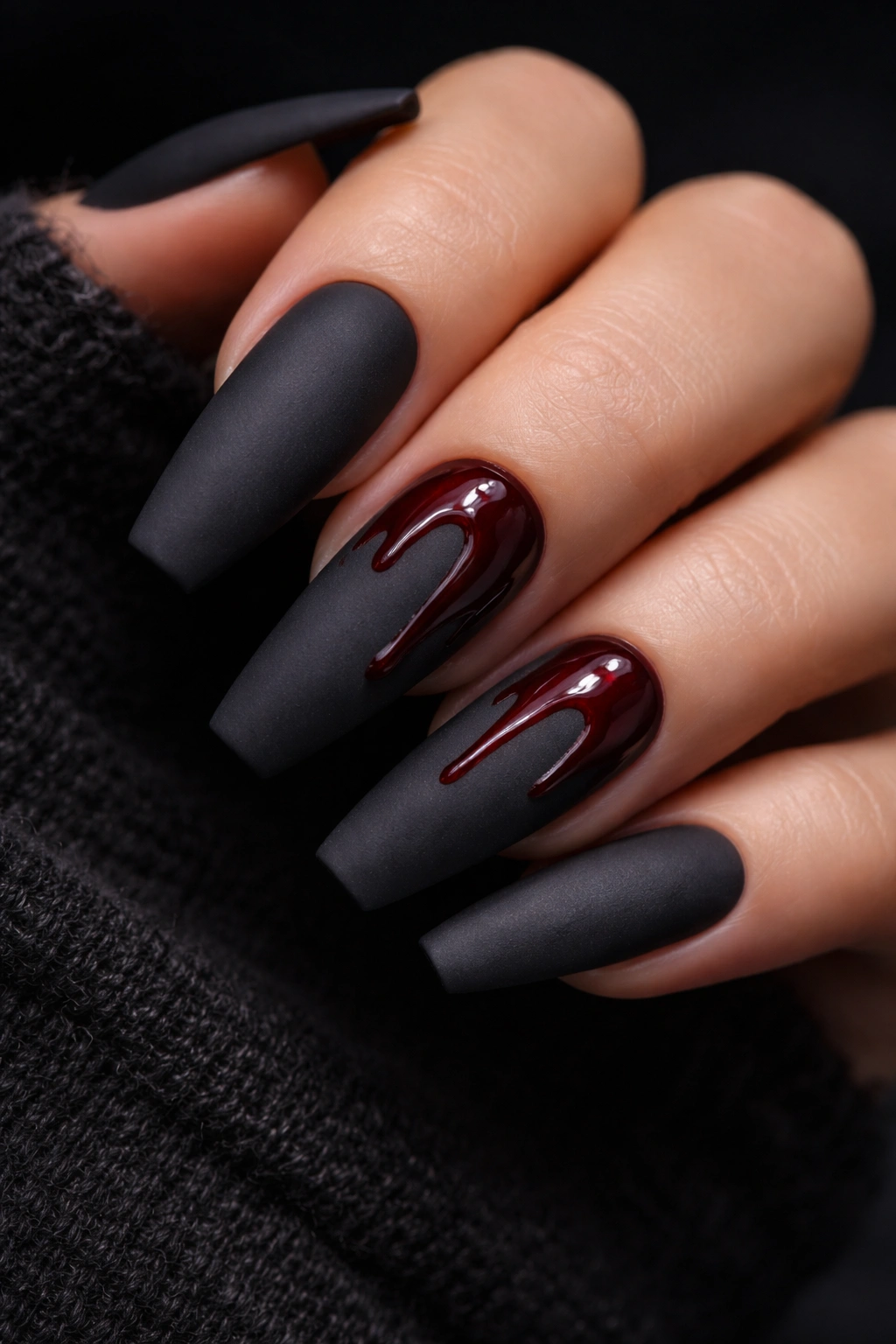 Close-up of matte charcoal nails with red drip art on two accent nails