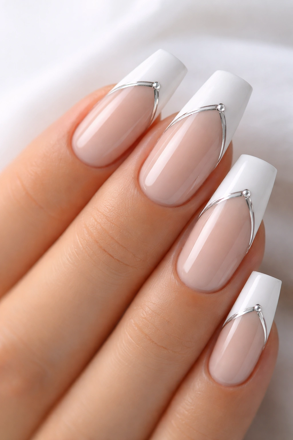 Close-up of coffin nails with matte white tips and metallic accents on a nude base