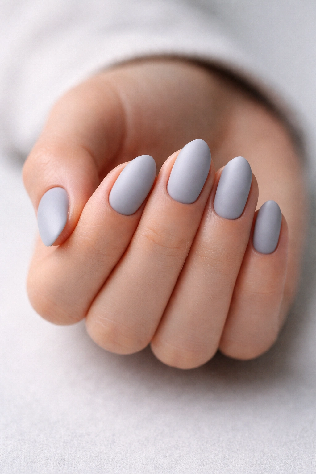 Close-up of matte fog gray short almond nails with icy undertone on neutral background