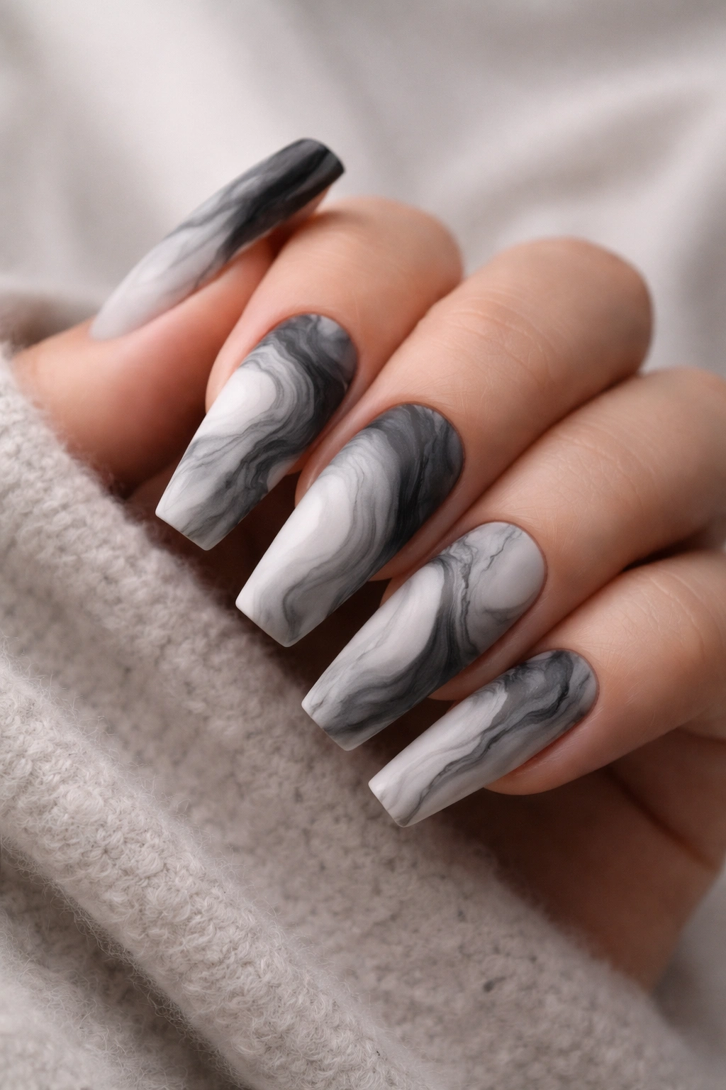 Close-up of matte marble nails with white gray black swirls on a hand