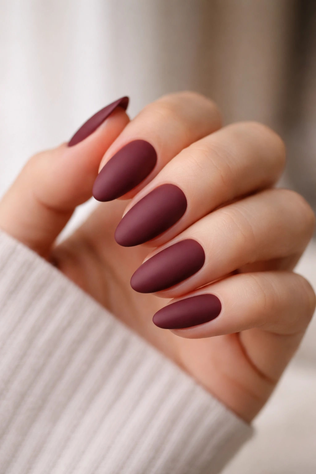 Close-up of short almond nails in matte merlot finish with soft focus