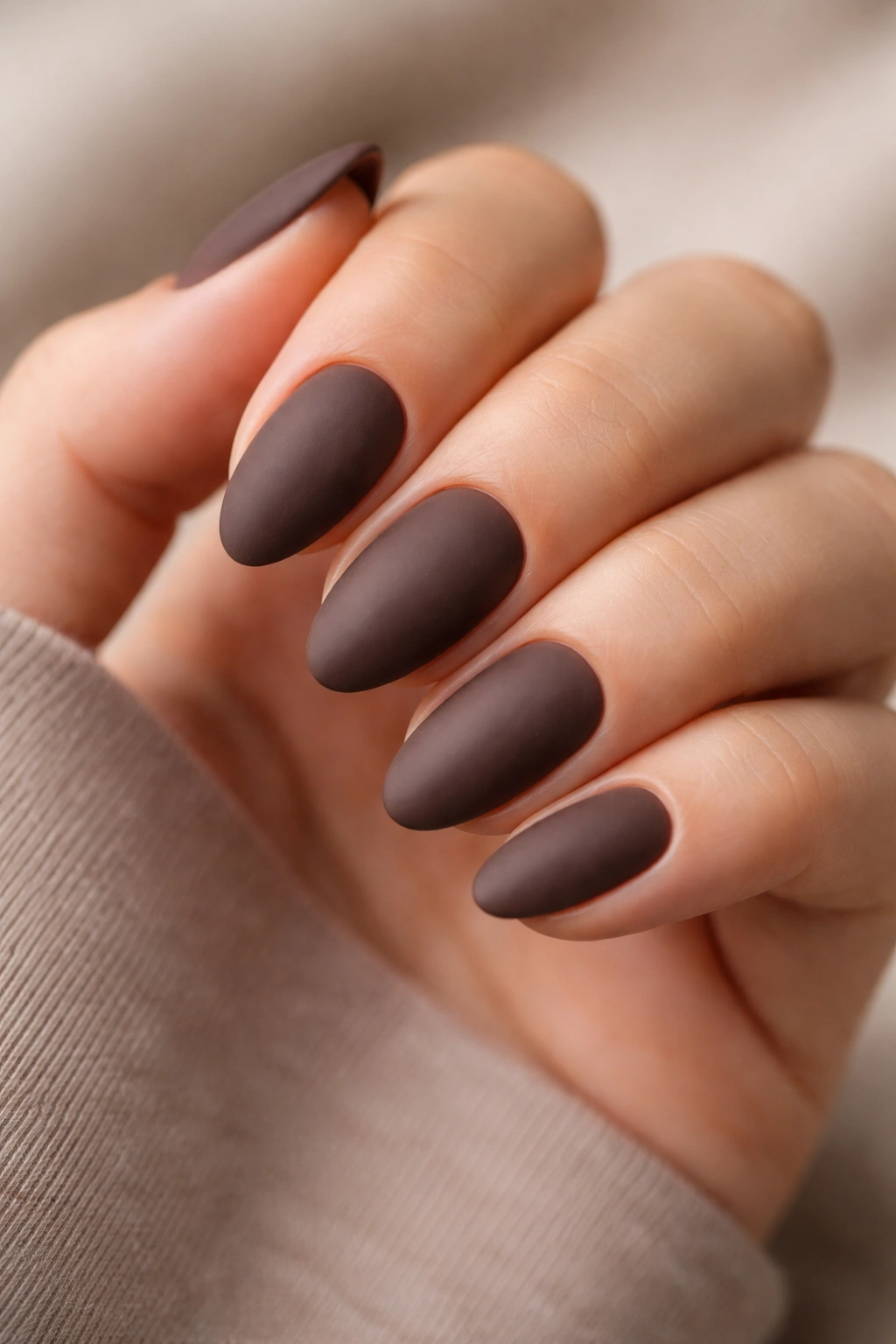 Close-up of short almond nails in matte mocha shade on bare hand