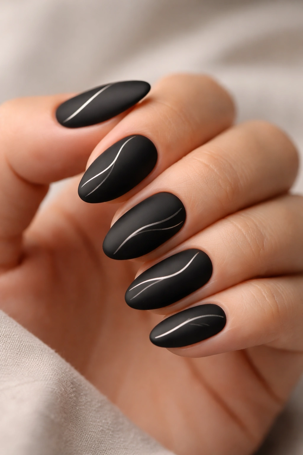 Close-up of matte black almond nails with a single abstract line