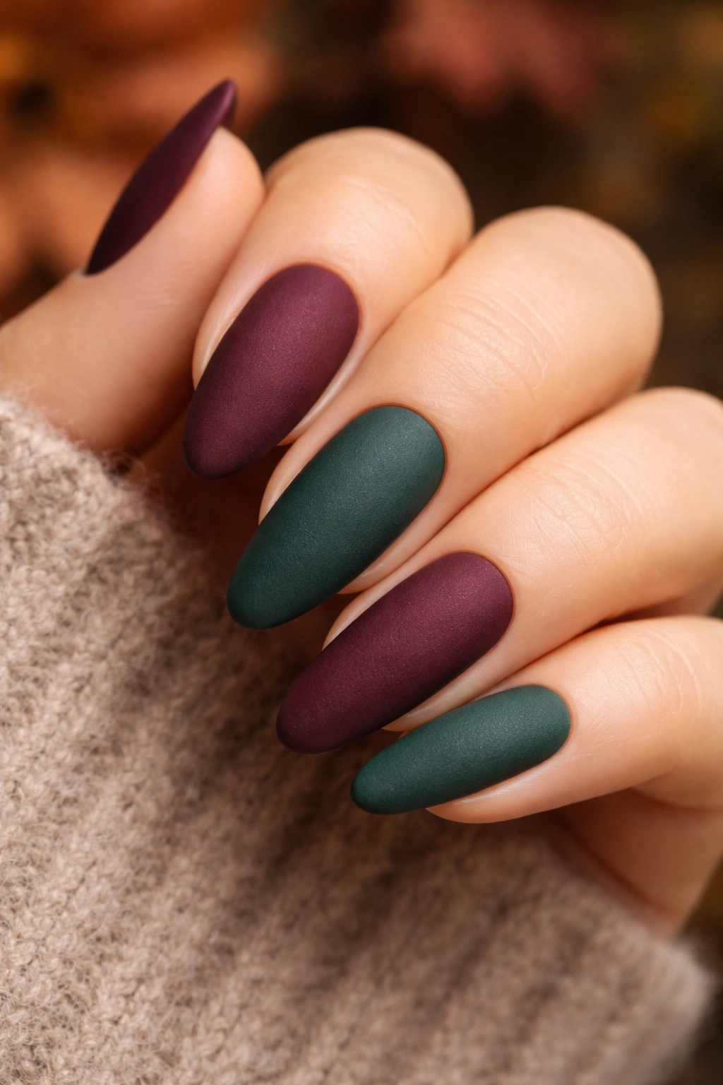 Close-up of matte-finish nails in burgundy and forest green with velvet texture