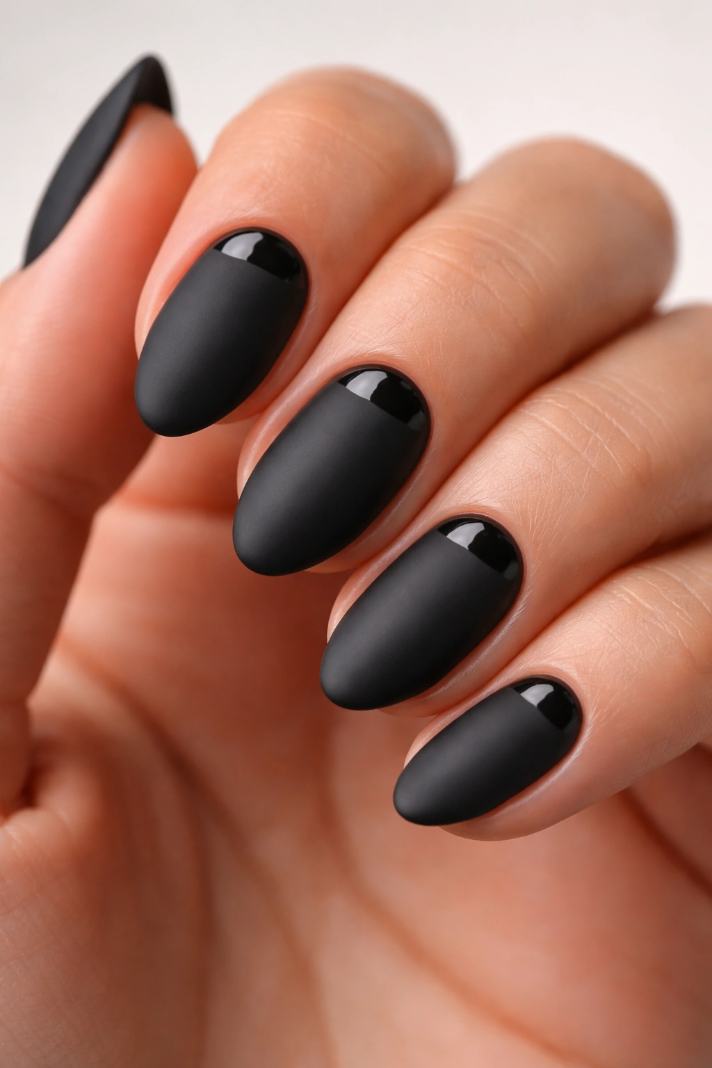 Close-up of matte black almond nails with a glossy crescent near the cuticle