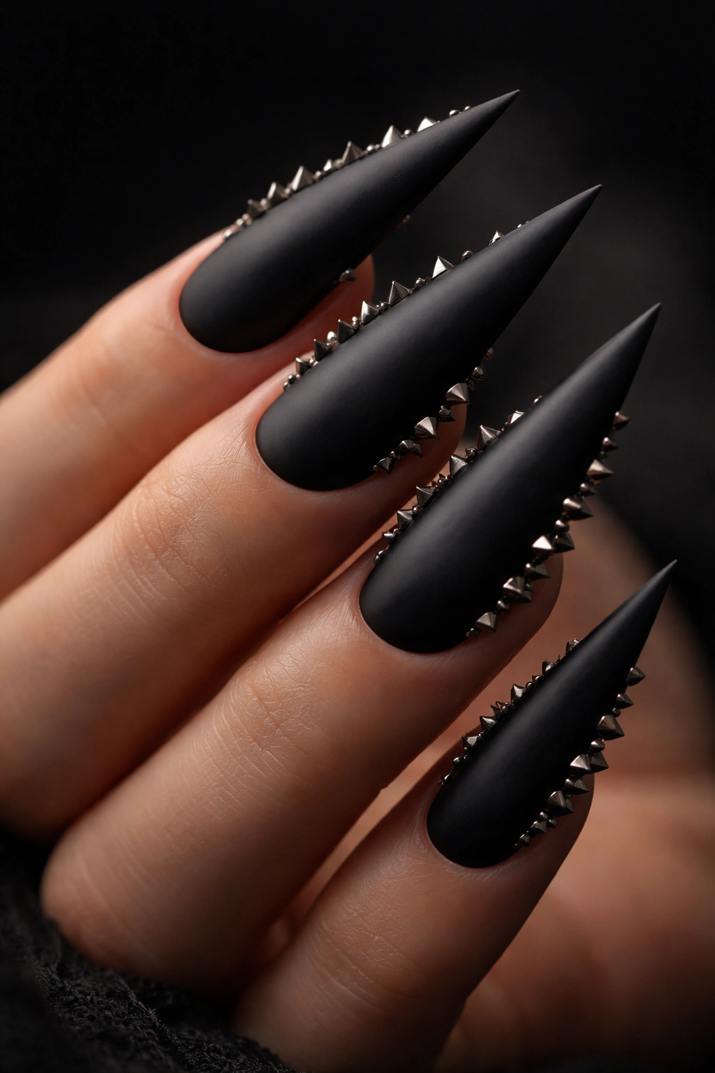 Close-up of matte black stiletto nails with dimensional spikes along the edges and tips.