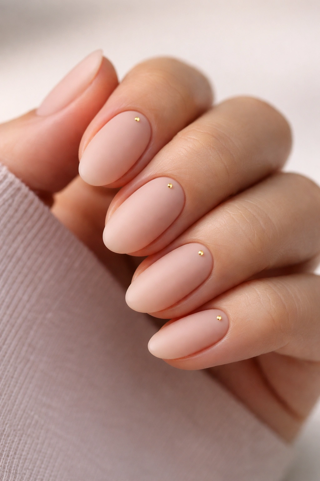Nude matte almond nails with tiny gold dots near cuticle