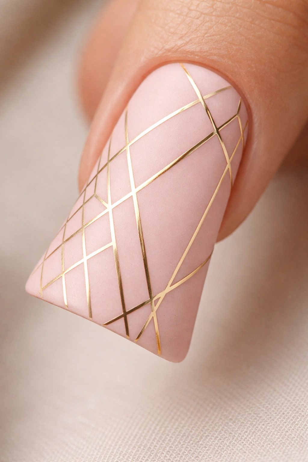 Close-up of a matte pink duck nail with gold geometric lines