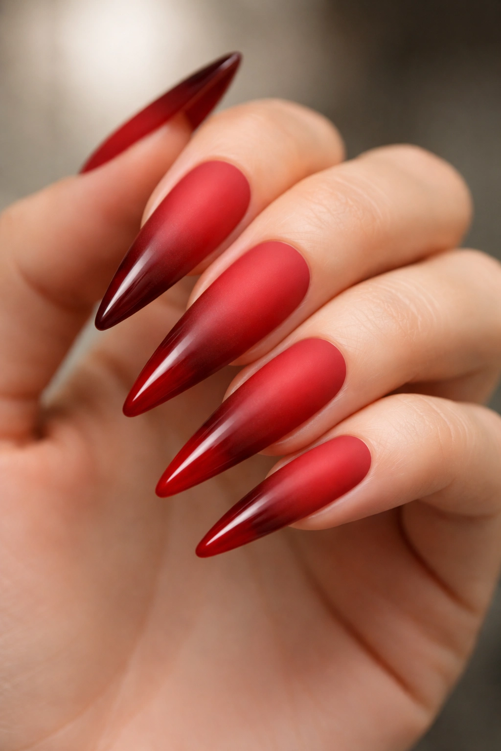 Close-up of matte-to-gloss red ombre stiletto nails on a hand