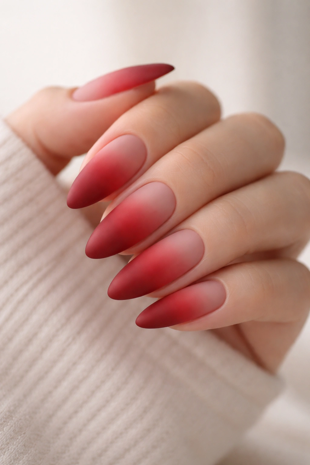 Close-up of matte red ombre almond nails with velvet finish