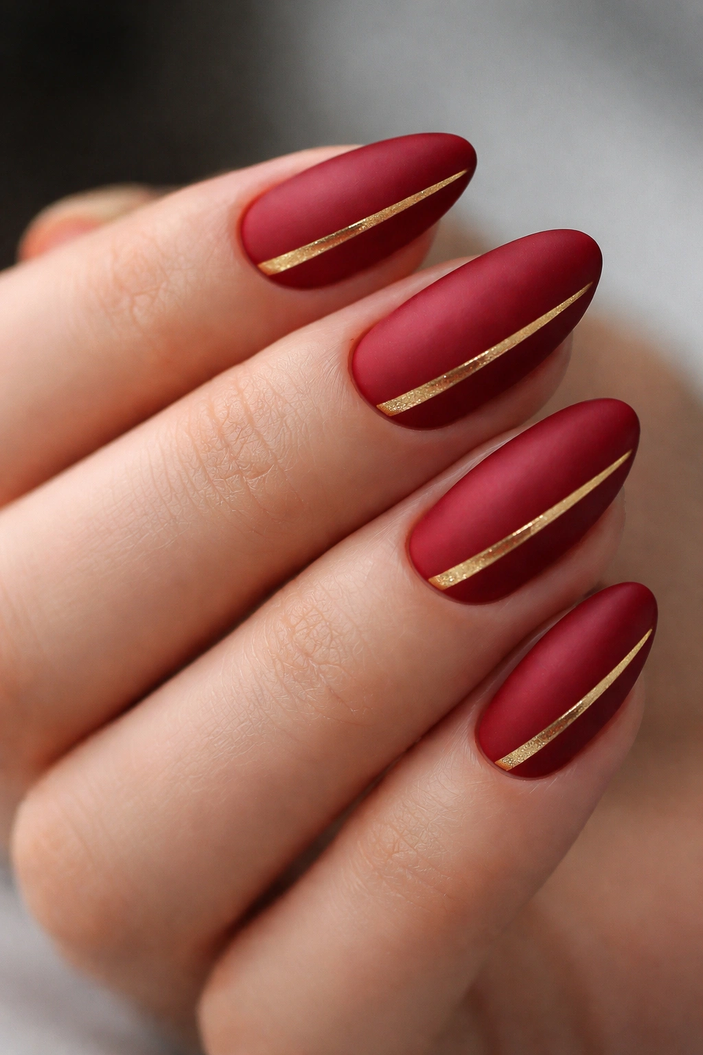 Close-up of matte cherry red nails with a thin gold stripe