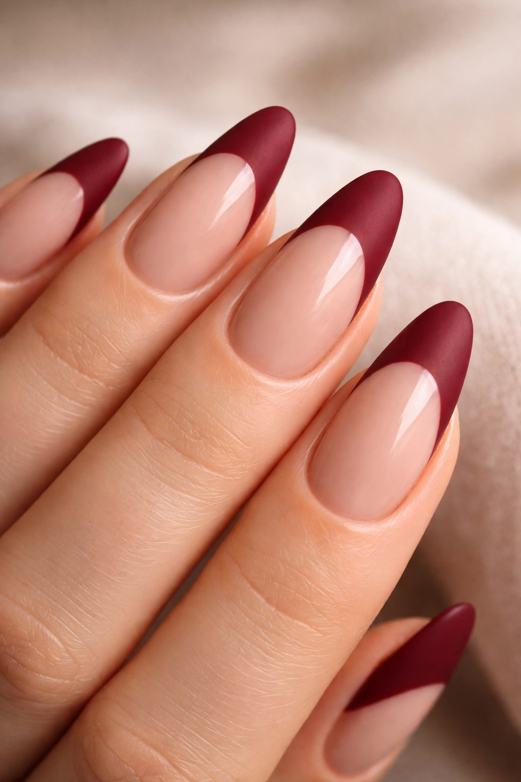 Close-up of almond nails with matte wine-red tips and glossy nude base