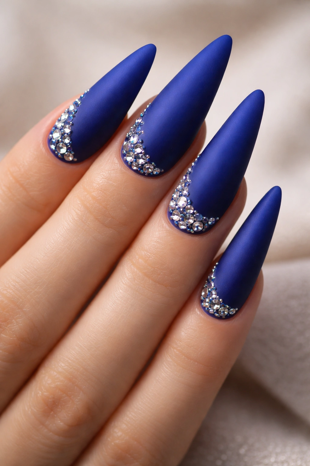 Matte royal blue stiletto nails with stones on a neutral background