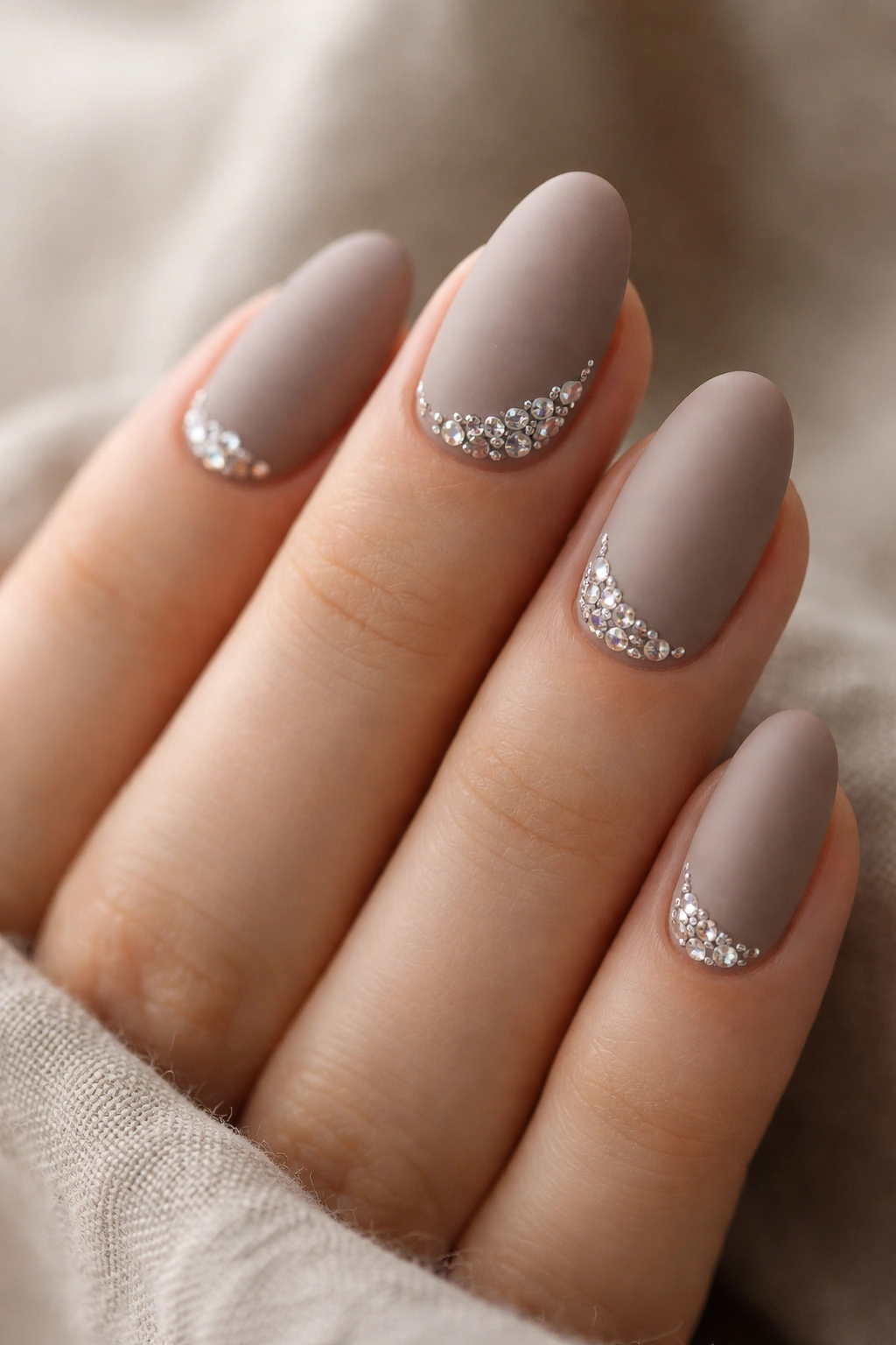 Close-up of matte taupe nails with glossy rhinestone clusters at the cuticle