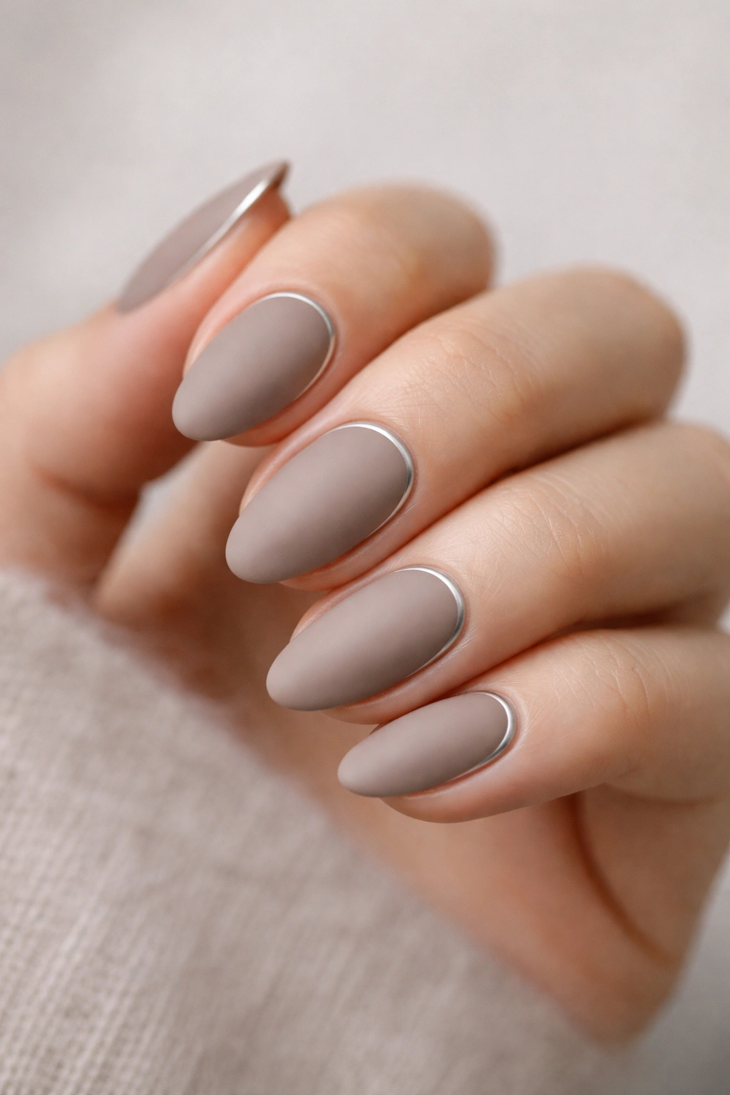 Close-up of matte taupe almond nails with a thin silver line