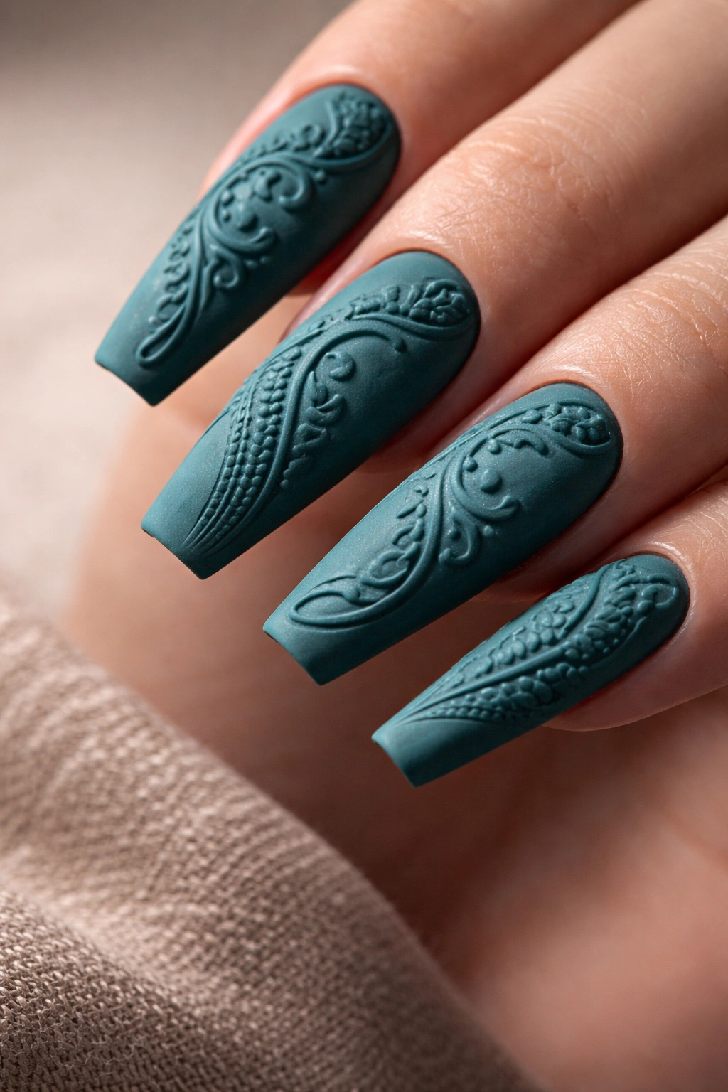 Close-up of coffin nails with matte teal base and embossed raised texture.