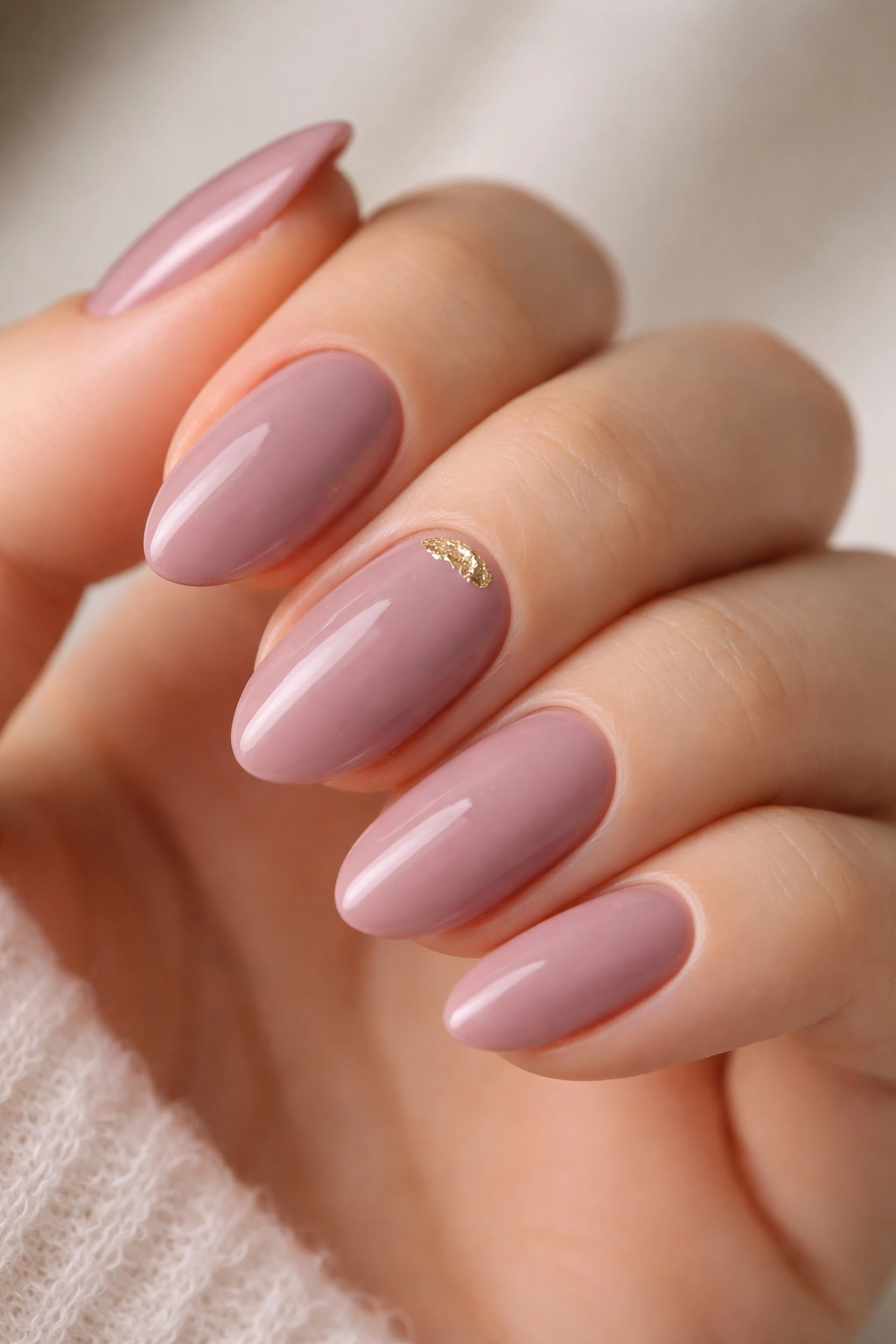 Close-up of mauve nails with a tiny gold foil accent near the cuticle on a short almond nail