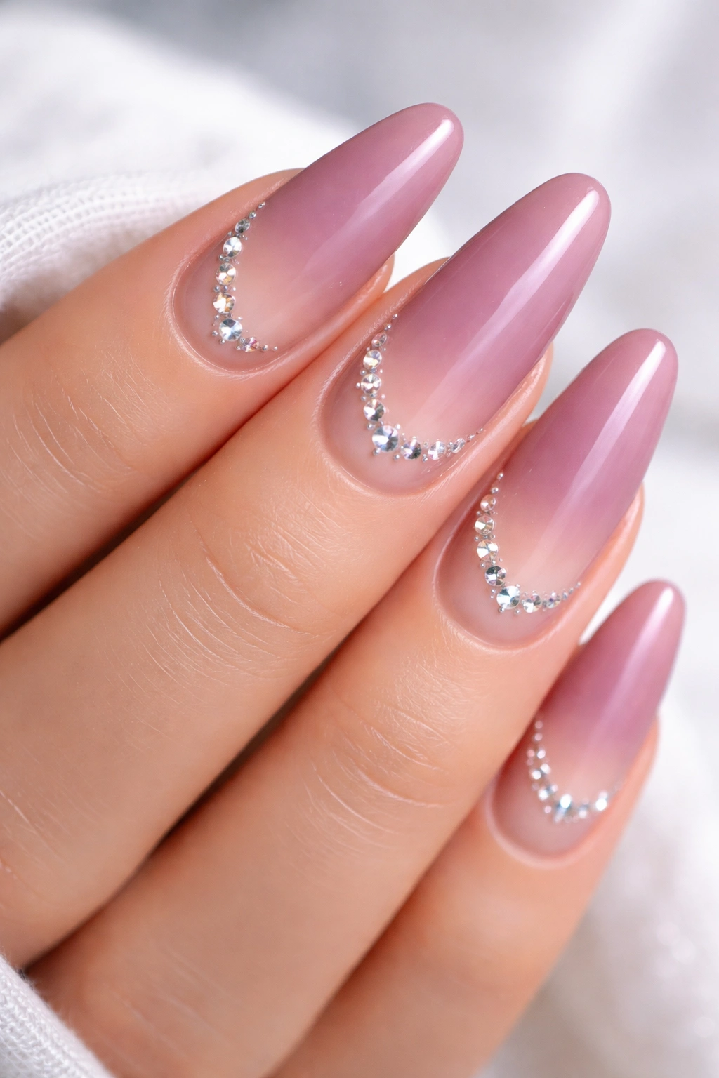 Close-up of long oval mauve-to-nude ombre nails with rhinestones
