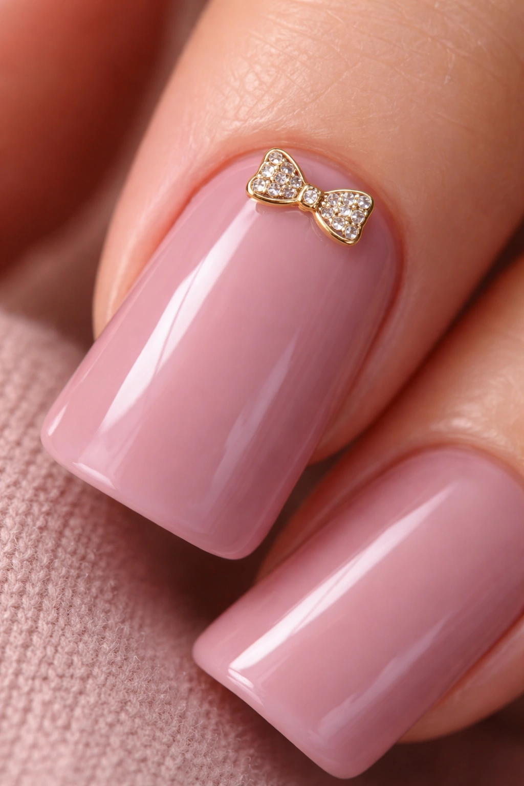Close-up of mauve pink nail with a small bow charm by the cuticle.