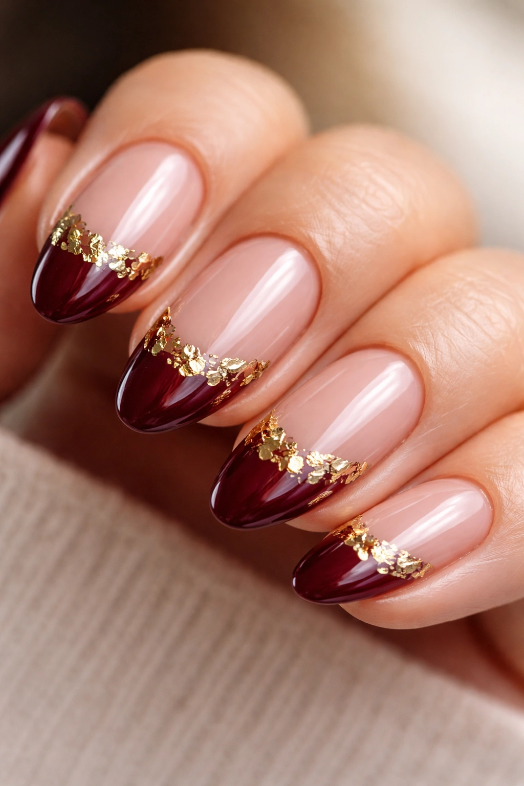 Close-up of short almond nails with deep merlot polish and gold foil accents along the smile line