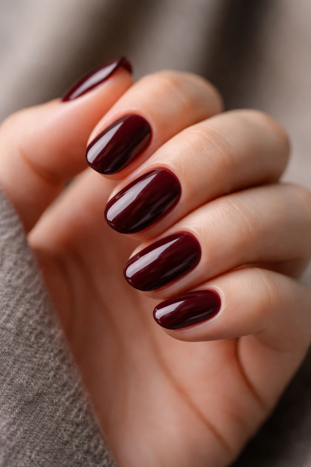 Close-up of short oval nails painted deep merlot with a glossy finish