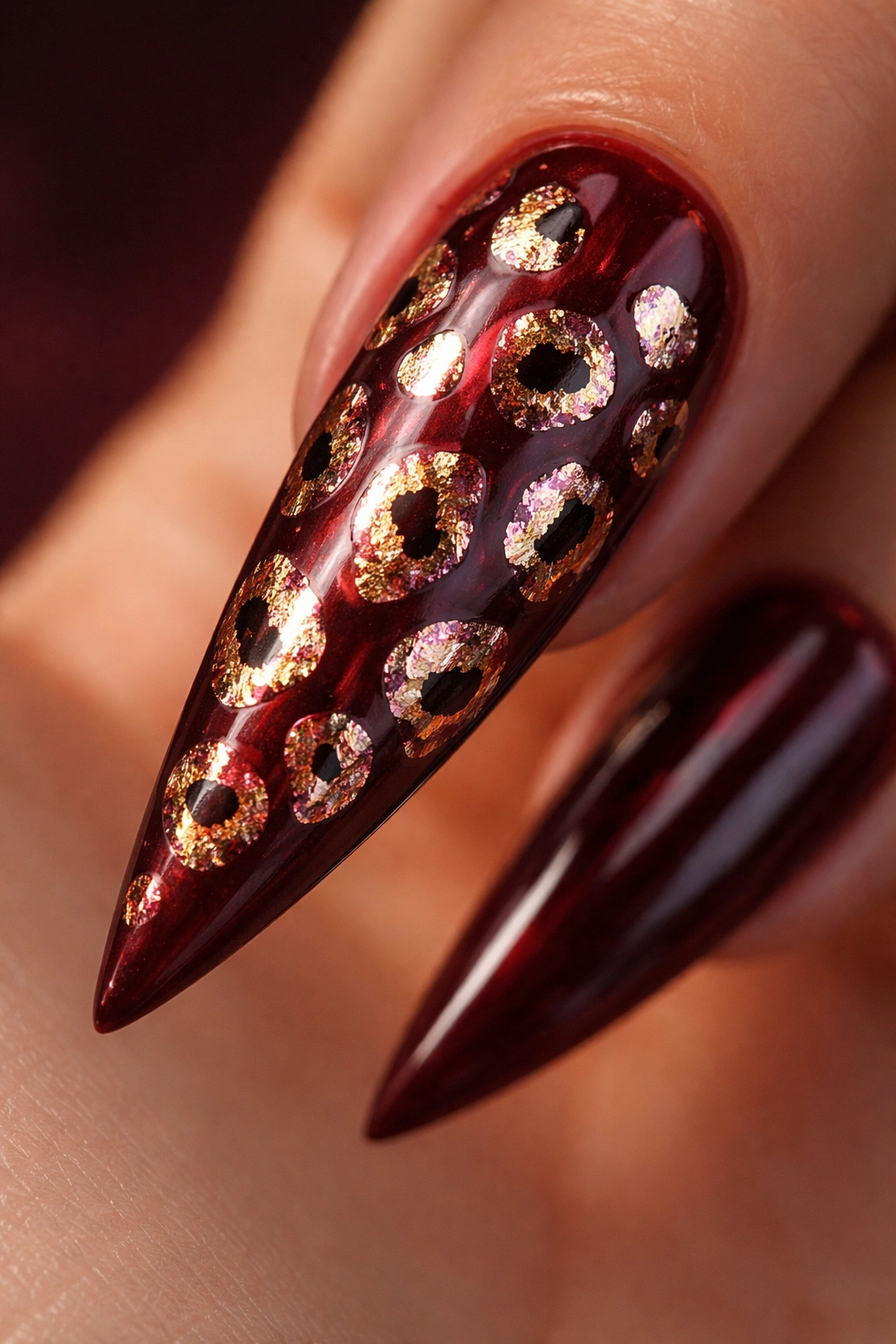 Stiletto nail with burgundy base and metallic cheetah spots reflecting light