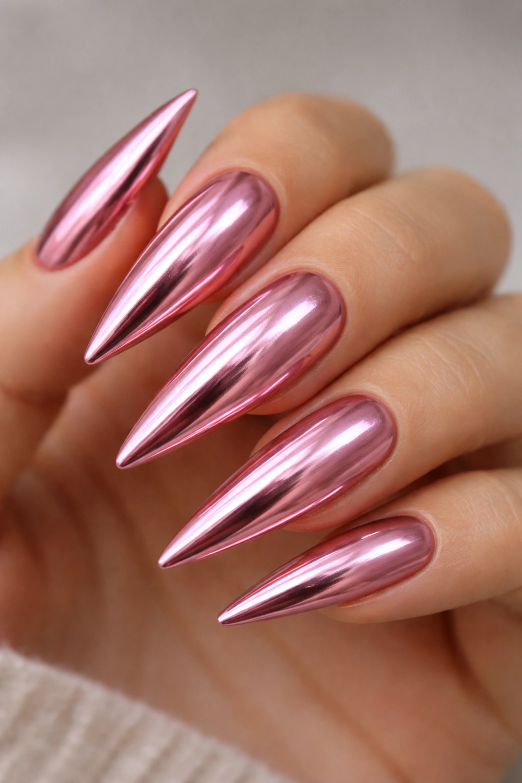 Close-up of metallic pink stiletto nails with rose-gold chrome finish